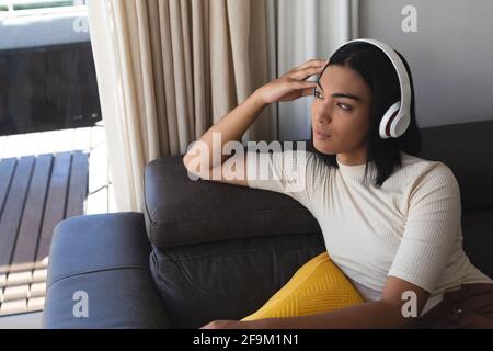 Bonne femme transgenre de race mixte se détendant dans le salon assis sur un canapé avec casque Banque D'Images