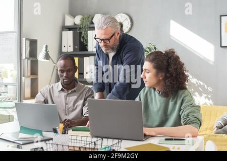 Professeur mature enseignant enseignant à ses étudiants pendant qu'ils sont assis à la table et travail sur les ordinateurs portables Banque D'Images