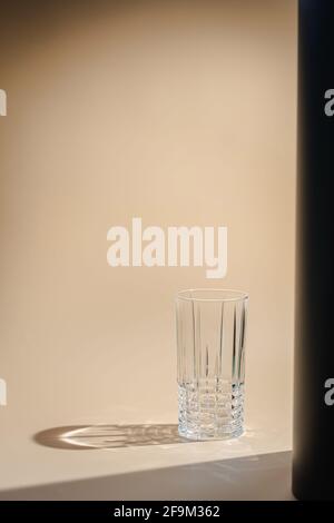 Le verre projette une magnifique ombre et un bel effet caustique lorsque la lumière traverse un verre. Reflet de l'ombre de la lumière du soleil sur fond orange clair Banque D'Images