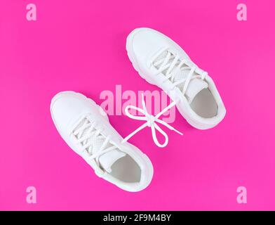 Paire de chaussures de sport blanches reliées par des lacets et ornées d'un noeud sur fond rose. Banque D'Images
