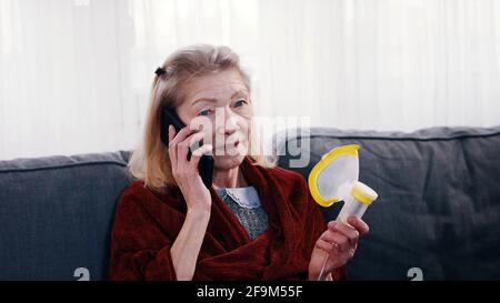 Femme solitaire âgée tenant un inhalateur d'oxygène et ayant un téléphone conversaion. Pandémie de Covid19. Photo de haute qualité Banque D'Images