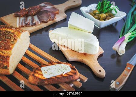 Fromage Haloumi avec pain fraîchement grillé aux oignons verts, jambon fumé, saucisse, olives sur une table à manger en bois sombre. Banque D'Images