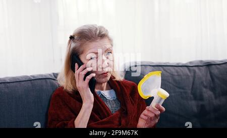 Femme solitaire âgée tenant un inhalateur d'oxygène et ayant un téléphone conversaion. Pandémie de Covid19. Photo de haute qualité Banque D'Images