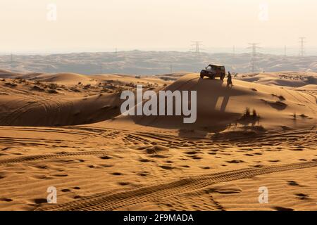 Silhouette de voiture 4x4 et d'homme arabe en vêtements traditionnels au sommet d'une dune de sable au coucher du soleil, Fossil Rock, Sharjah, Émirats arabes Unis. Banque D'Images
