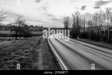 Vide route courbe menant à l'horizon dans la campagne, monochrome. Bad Friedrichshara, sud de l'Allemagne. Scène dramatique. Banque D'Images