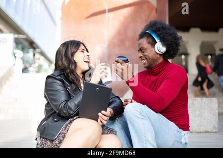 Une femme caucasienne et un homme afro-américain qui boit du café à l'extérieur. Ils rient très heureusement. Espace pour le texte. Banque D'Images