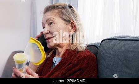 Femme âgée utilisant un inhalateur d'oxygène tout en ayant un appel téléphonique. Personne vulnérable pendant l'épidémie de covid. Photo de haute qualité Banque D'Images