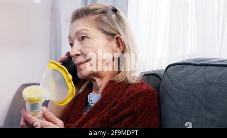 Une vieille femme vulnérable ayant un appel téléphonique et utilisant un inhalateur. Difficulté à respirer à la vieillesse. Photo de haute qualité Banque D'Images