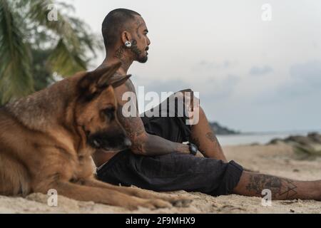 homme asiatique assis sur la plage avec un chien parmi les palmiers Banque D'Images