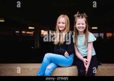 Deux filles joyeuses entre elles assises sur un mur de briques ensemble. Banque D'Images