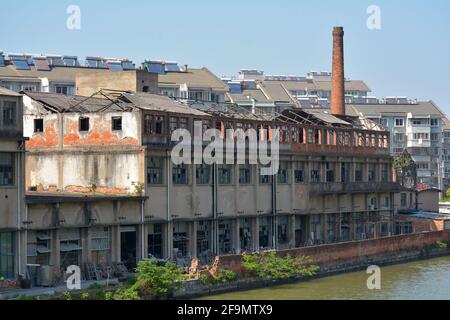 Grand complexe d'usine avec grande cheminée en brique abandonnée et la plupart du temps abandonnée sur le bord d'un canal. Flanqué de blocs d'appartements modernes. Banque D'Images