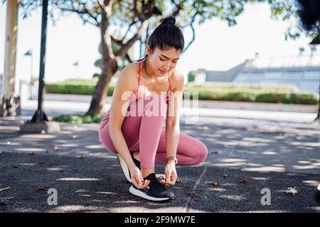 Jeune femme asiatique de tenue sportive nouant des lacets de chaussures de course à pied en vous faisant de l'activité dans un parc extérieur et en faisant une pause entre les deux formation à l'air frais Banque D'Images