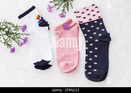 Trois paires de chaussettes et de fleurs pour femmes sur fond blanc structuré, vue du dessus. Banque D'Images