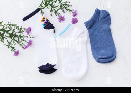 Trois paires de chaussettes et de fleurs pour femmes sur fond blanc structuré, vue du dessus. Banque D'Images