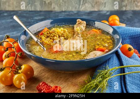 Soupe aux pois avec poulet, carottes, tomates et herbes dans une assiette profonde sur bois avec serviette sur fond bleu. Banque D'Images
