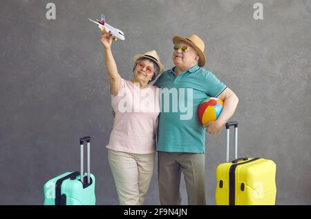 Photo de studio d'un couple senior heureux en lunettes de soleil et chapeaux tenir un avion en papier Banque D'Images