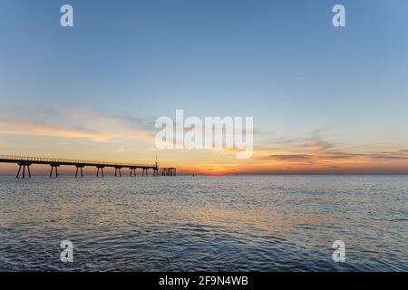 Tôt le matin quelques minutes avant le lever du soleil. Aube sur la mer avec ponton. Le ciel bleu est peint dans des tons d'orange. Banque D'Images