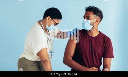 Femme médecin donnant le vaccin à un homme pendant une pandémie. Professionnel de la santé et homme portant des masques protecteurs pendant la vaccination. Banque D'Images