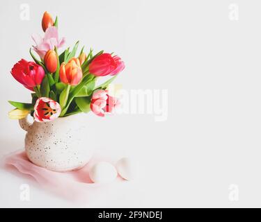 Composition de Pâques avec tulipes multicolores dans une carafe, œufs blancs sur fond blanc avec espace de copie. Préparation pour Pâques. Ambiance de vacances de printemps. FLO Banque D'Images