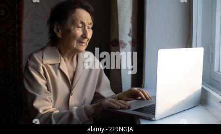 Une femme âgée heureuse assise avec sa petite-fille regardant un ordinateur portable passer un appel vidéo. Femme d'âge mûr parlant à la webcam, faisant le chat en ligne à la maison pendant Banque D'Images