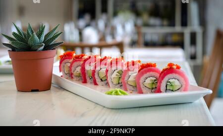 Délicieux sushi japonais, rouleau de californie uramaki et roulé d'avocat de thon sur une assiette blanche, servi avec de la sauce de wasabi et de soja et décoré avec de l'aloès Banque D'Images