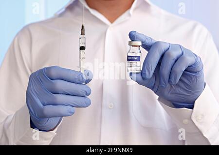 Gros plan des mains du médecin dans des gants en latex bleu montrant le nouveau flacon de vaccin Covid-19 et surrempli de médicaments. Gros plan, espace de copie, retour arrière Banque D'Images