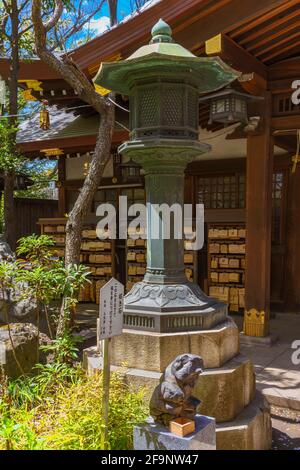 tokyo, japon - avril 09 2021 : lanterne en cuivre et monument en pierre Maneki-ishi représentant la forme d'un chat de fortune manekineko japonais que les croyants peuvent Banque D'Images