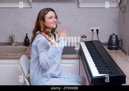 Une femme dans une chemise de nuit bleue semble surprise la répandre mains tout en étant assis au piano dans la cuisine Banque D'Images