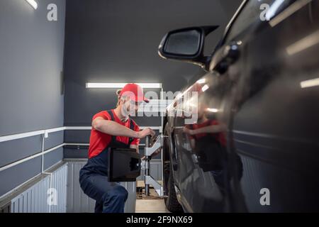 Travailleur dans une combinaison près de la roue de la voiture Banque D'Images