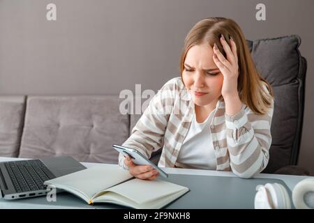 Jeune femme bouleversée sous le stress. Une femme confuse tenant la tête a reçu de mauvaises nouvelles au travail via un smartphone. Une jeune fille regarde l'écran du smartphone pendant onli Banque D'Images