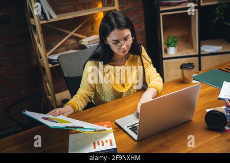 Jeune femme travaillant dans un bureau moderne utilisant des appareils et des gadgets. Création de rapports, d'analyses, de tâches de traitement de routine Banque D'Images