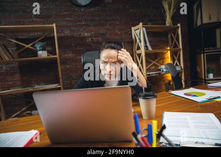 Jeune femme travaillant dans un bureau moderne utilisant des appareils et des gadgets. Création de rapports, d'analyses, de tâches de traitement de routine Banque D'Images