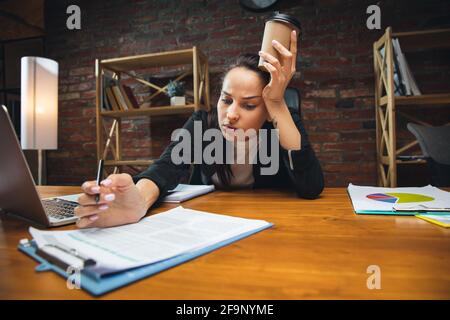 Jeune femme travaillant dans un bureau moderne utilisant des appareils et des gadgets. Création de rapports, d'analyses, de tâches de traitement de routine Banque D'Images