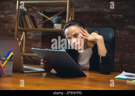 Jeune femme travaillant dans un bureau moderne utilisant des appareils et des gadgets. Création de rapports, d'analyses, de tâches de traitement de routine Banque D'Images
