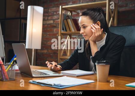 Jeune femme travaillant dans un bureau moderne utilisant des appareils et des gadgets. Création de rapports, d'analyses, de tâches de traitement de routine Banque D'Images