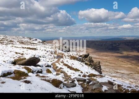 Chemin le long du bord nord de Kinder Scout en regardant vers le bas sur les landes de Pennine avec un mélange inhabituel de neige et le soleil d'avril. Banque D'Images