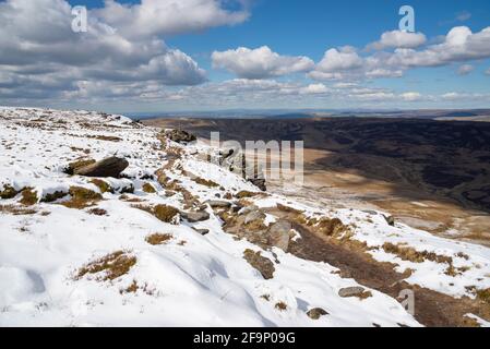 Chemin le long du bord nord de Kinder Scout en regardant vers le bas sur les landes de Pennine avec un mélange inhabituel de neige et le soleil d'avril. Banque D'Images