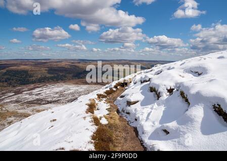 Chemin le long du bord nord de Kinder Scout en regardant vers le bas sur les landes de Pennine avec un mélange inhabituel de neige et le soleil d'avril. Banque D'Images