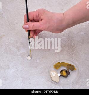 Une femme âgée peint un ornement avec une brosse sur un carreau de sol endommagé. Peinture pour la reconstruction de la surface du sol dans la maison Banque D'Images