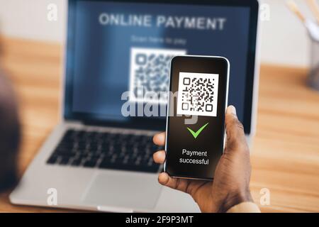 Black man scannant le code qr à partir d'un ordinateur portable avec smartphone Banque D'Images