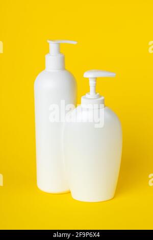 Deux bouteilles en plastique sur fond jaune, ensemble de récipients cosmétiques avec distributeur. Produits de toilette, lotion à pompe. Crème hydratante pour le corps et le visage. Banque D'Images