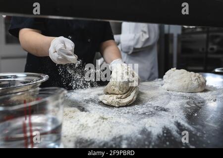 Milieu de la pâte à pétrir d'un chef professionnel portant des gants hygiéniques. Travail dans une cuisine de restaurant très fréquentée. Banque D'Images