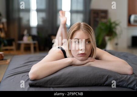Jeune femme blonde allongé sur un oreiller avec une vue pensive pendant son temps libre à la maison Banque D'Images