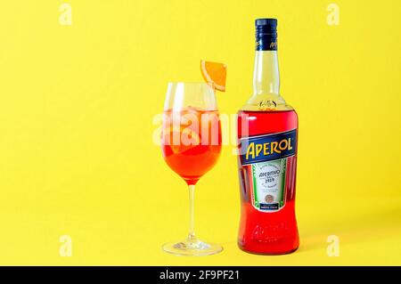 Lugansk, Ukraine - 29 mars 2021 : cocktail Aperol Spritz. Apéritif en bouteille et verre à vin avec glace sur fond jaune. Longue boisson gazeuse. CR minimale Banque D'Images