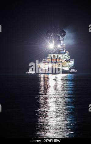 vue nocturne d'un bateau de pêche éclairé se reflétant sur l'eau dans la baie de naples en italie. Banque D'Images