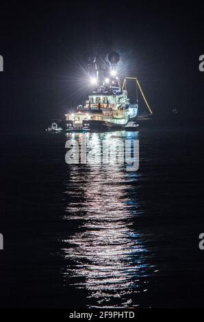 vue nocturne d'un bateau de pêche éclairé se reflétant sur l'eau dans la baie de naples en italie. Banque D'Images