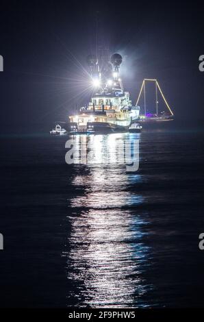 vue nocturne d'un bateau de pêche éclairé se reflétant sur l'eau dans la baie de naples en italie. Banque D'Images