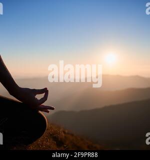 Gros plan des mains de la femme sur fond d'aube dans la soirée. Jeune femme faisant de l'exercice de yoga et méditant pendant le coucher du soleil dans les montagnes Banque D'Images