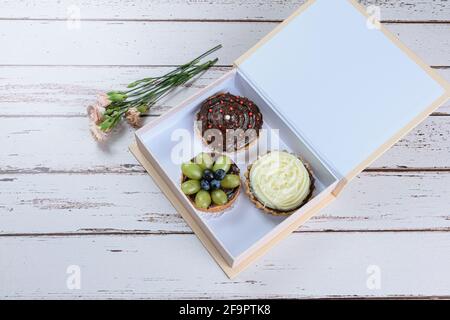 Tartes à la pâte de beurre farcies de ganache au chocolat avec diverses garnitures, à l'intérieur d'une boîte cadeau et à côté de roses. Banque D'Images