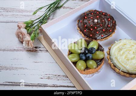 Gros plan de tartes avec pâte de beurre farcie de ganache au chocolat avec garnitures assorties, à l'intérieur d'une boîte cadeau et à côté de roses. Banque D'Images